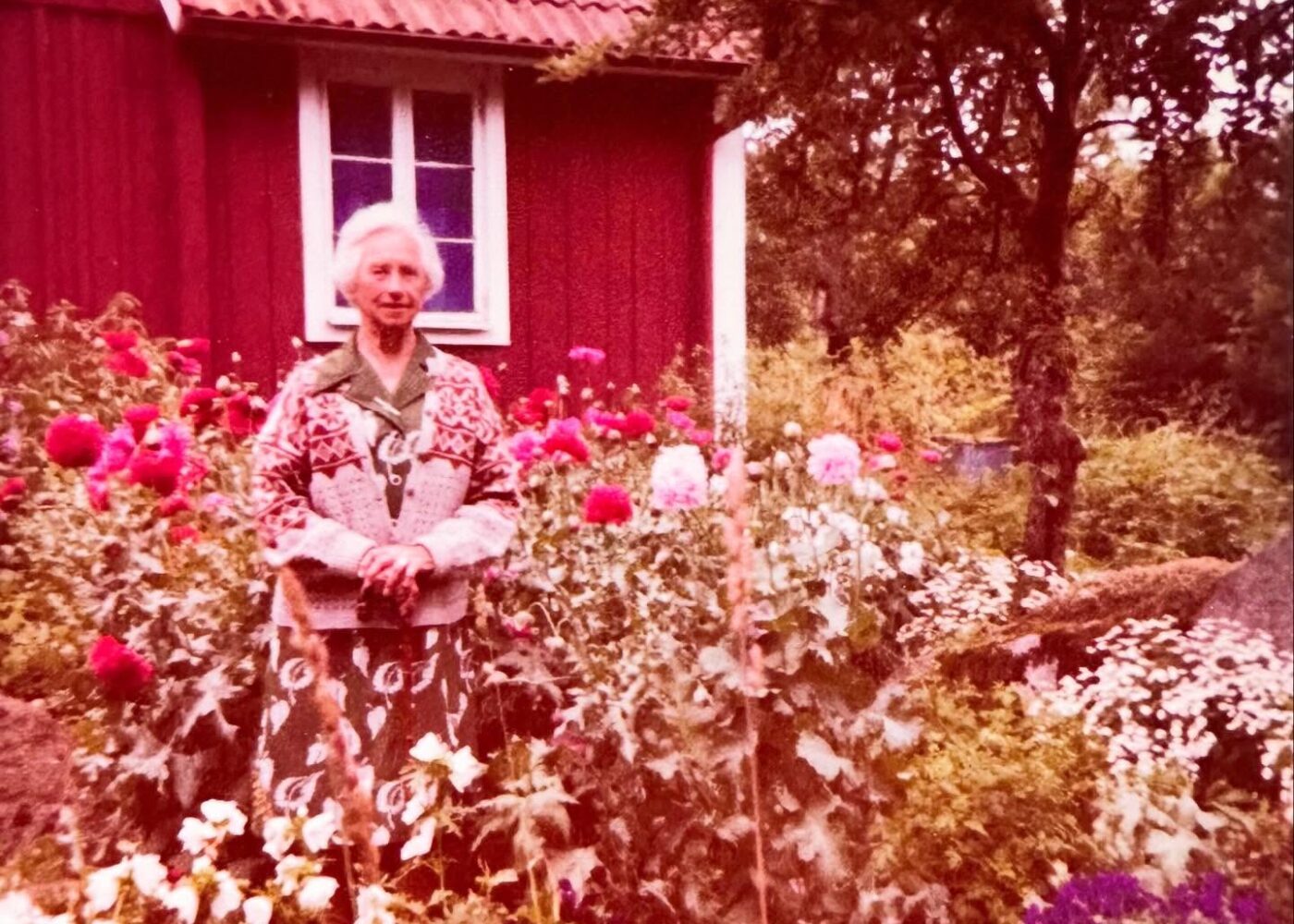 Alexandra Oakley's great-grandmother standing among flowers outside a red cottage